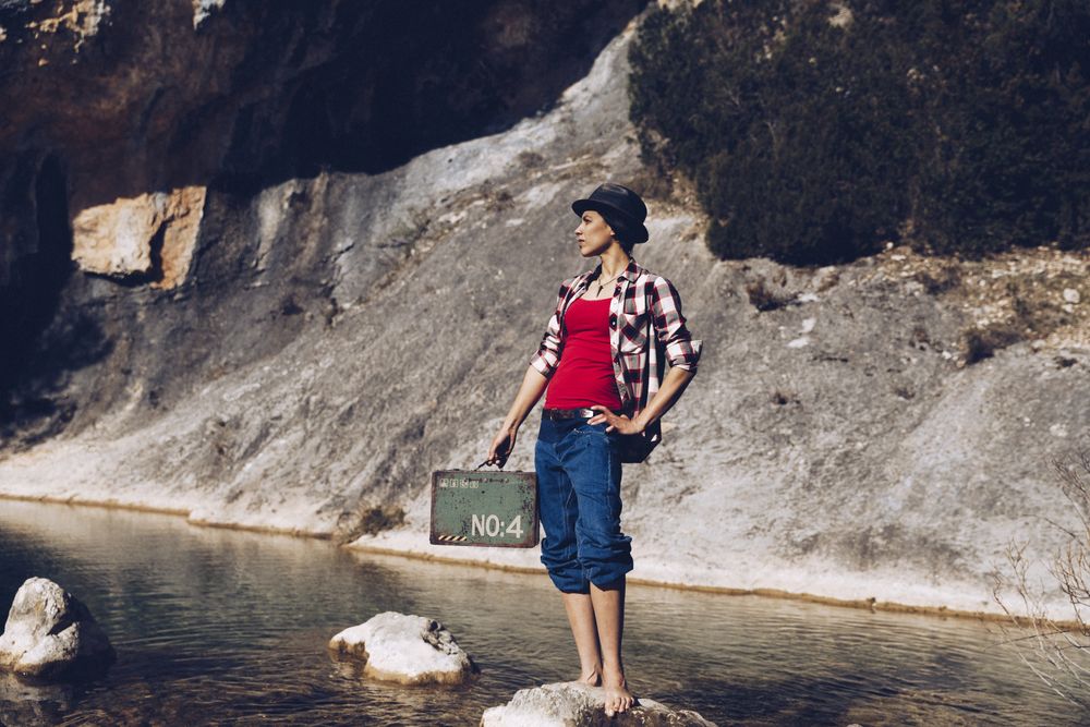 woman standing on rock with case near clear water in lake
