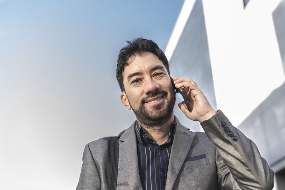 Low-angle view of an businessman talking on the cell phone while looking at camera in the street.