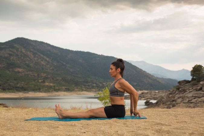Woman practicing yoga outdoors near water
