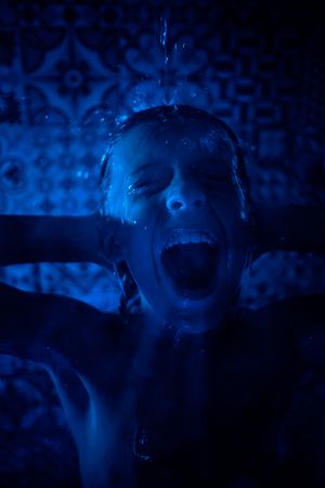 Shirtless boy shouting in shower room in blue light
