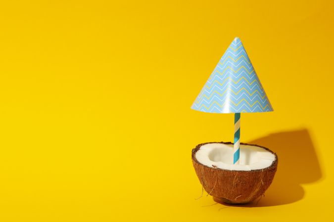 Coconut with beach umbrella on yellow background, space for text