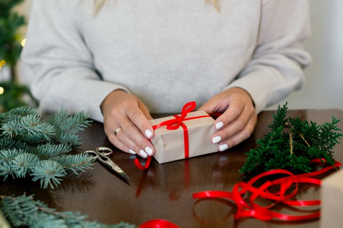 An unrecognizable woman is wrapping a Christmas gift in craft paper and a fir branch