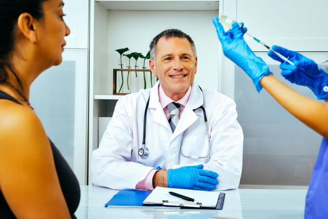 Medical assistant prepping vaccination for patient in smiling doctor’s office