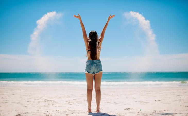 Young woman throwing sand in the air at the beach