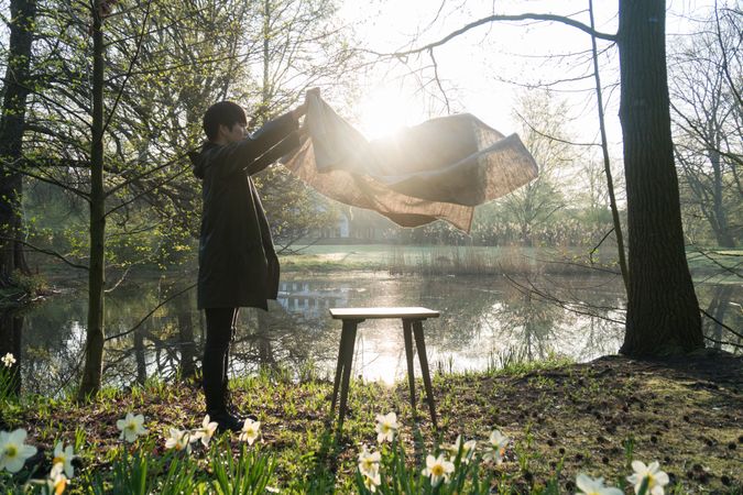 Man putting a table linen on a wooden table beside river and trees