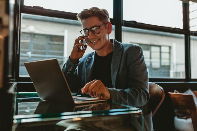 Smiling businessman with laptop talking on cellphone at office