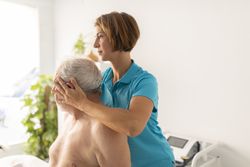 A female physiotherapist performs stretches on the neck of her mature male patient