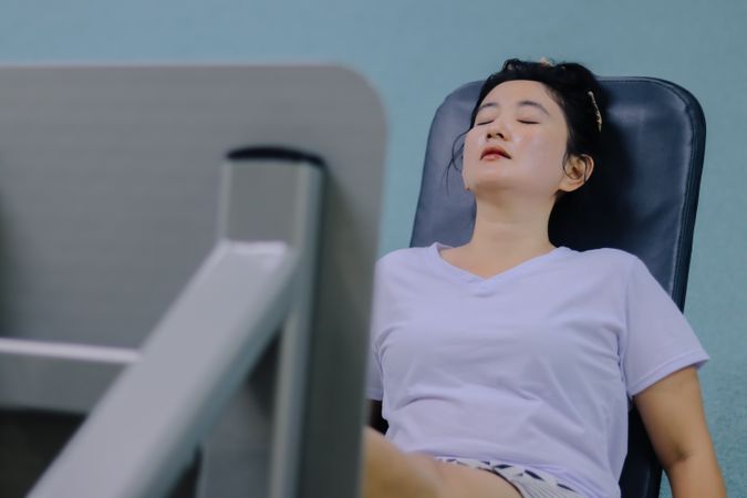 woman sitting on leg press machine, eyes closed, taking a break during workout session.