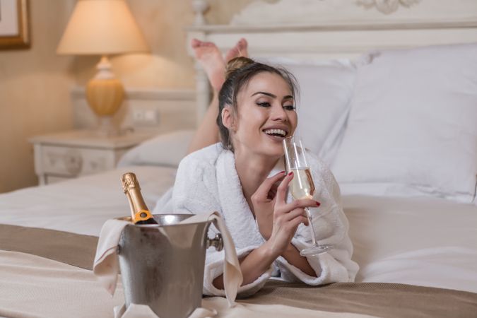 Woman in bathrobe laying forward enjoying a glass of champagne