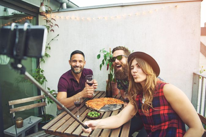 Three happy friends taking a selfie on a rooftop patio with pizza