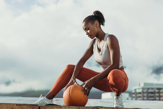 Athletic woman squatting and looking down at orange ball