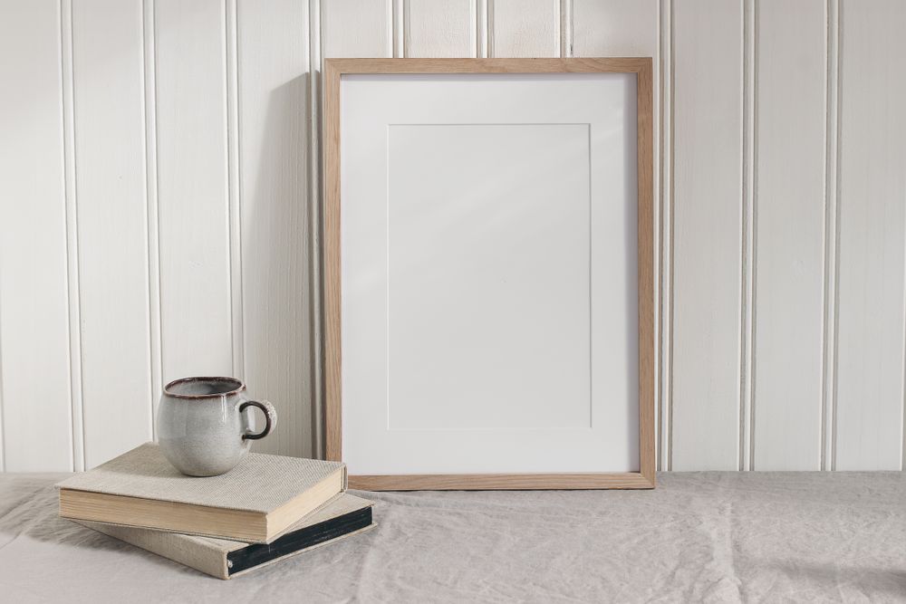 Blank vertical wooden picture frame mock up on linen table cloth. Modern interior. Cup of coffee on pile of vintage books.
