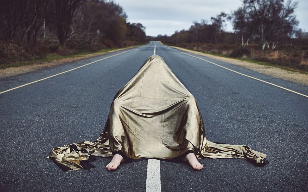 Man sitting in center of road under gold sheet