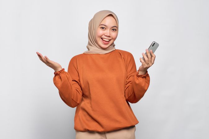 Muslim woman smiling with open gesture and holding smartphone