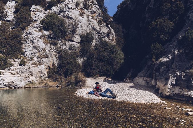 Positive woman and man resting on stone shore near river