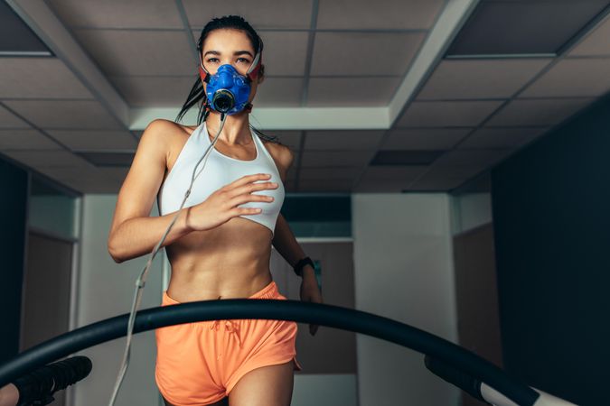 Fit woman running on treadmill with a mask checking her performance