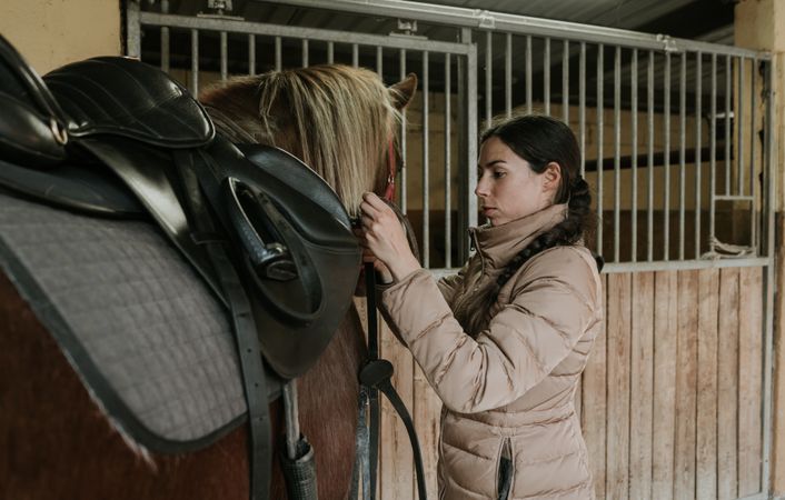 Woman putting saddle on horse
