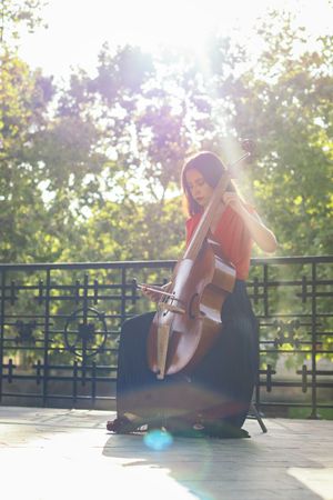 A young woman playing the cello on an outdoor stage