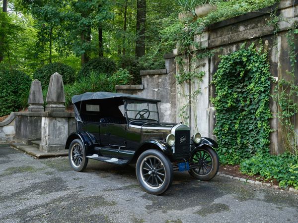 Antique Model T Ford parked by gray stone mansion
