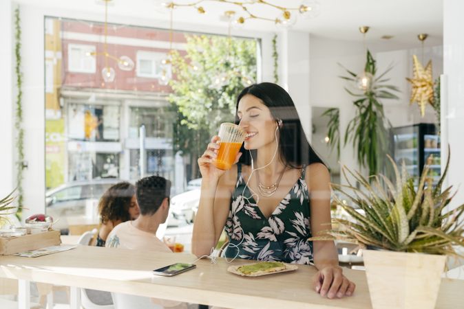 Woman with healthy drink listening to music in cafe