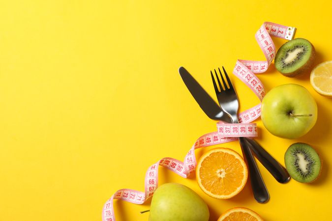 Cutlery, measuring tape and fruits on yellow background