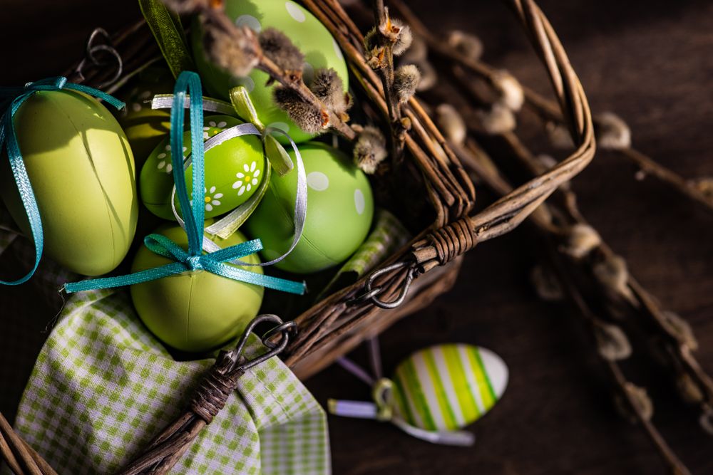 Top view of colorful eggs in basket and pussy willow branches on wooden table