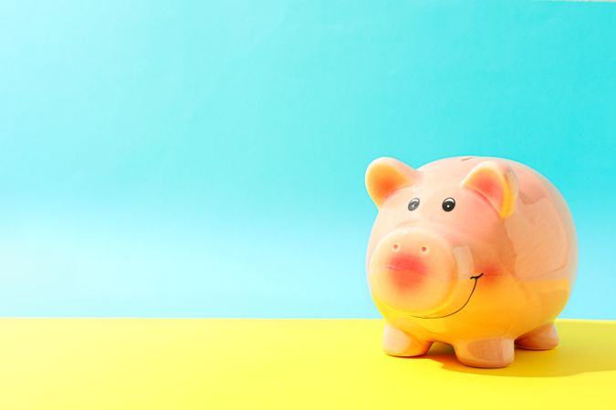 Happy piggy bank on yellow table against color background, space for text. Finance, saving money