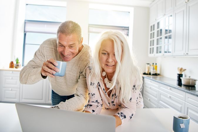 Happy older couple looking at  a laptop together at breakfast in their kitchen