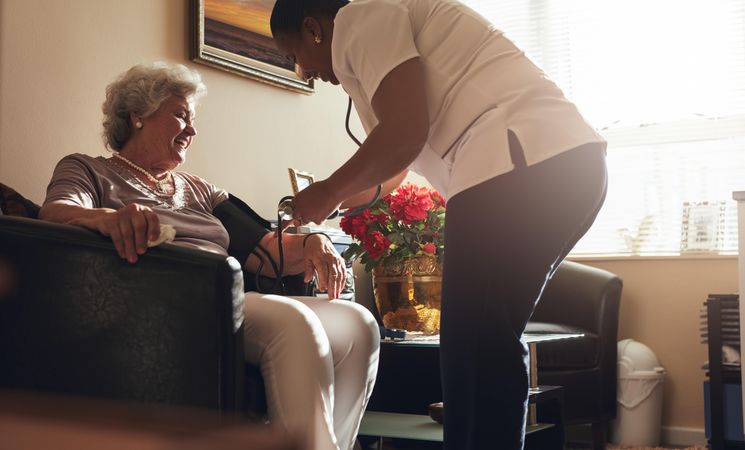Nurse taking blood pressure of older patient at home