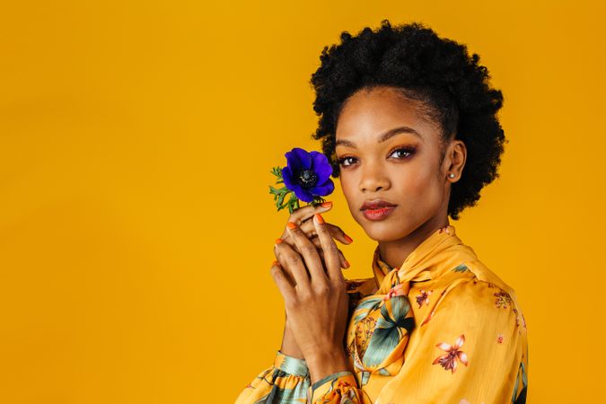 Serious Black woman holding blue flower to her face