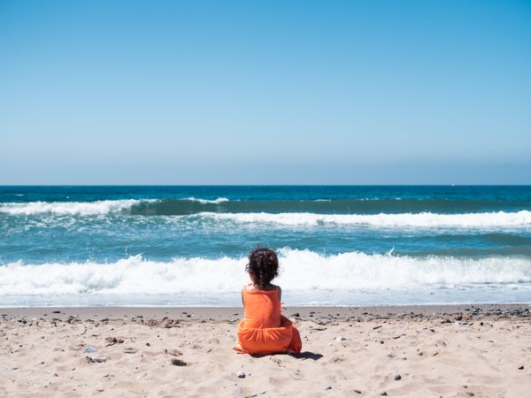 Little girl sitting on beach and admiring view