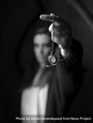 A young woman, out of focus, holds a pocket watch on a chain, and shows it hanging in the air, while time passes 0gXXlM