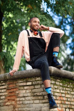 Smiling male sitting with one leg up on brick wall in city