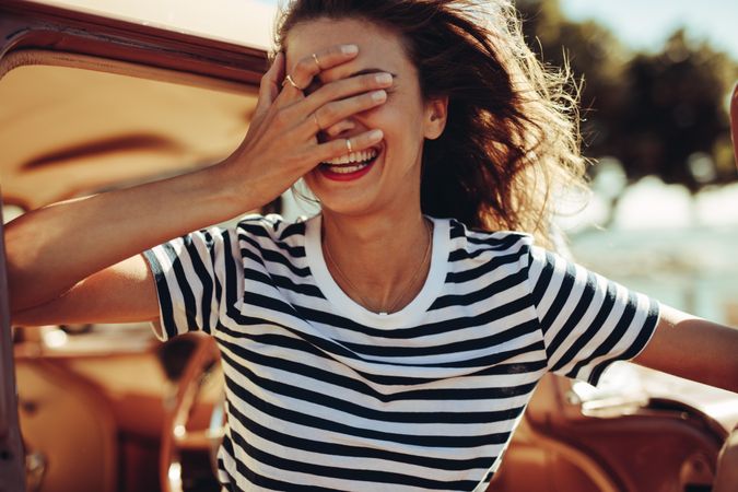 Woman laughing with her hand over her eyes in front of a vintage car