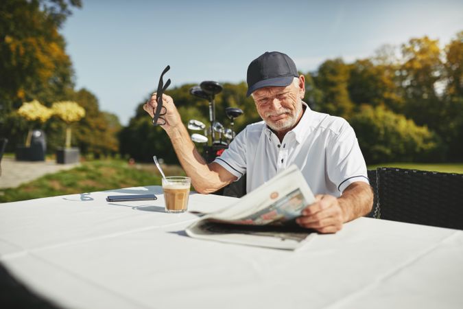 Man relaxing at golf course with coffee & newspaper