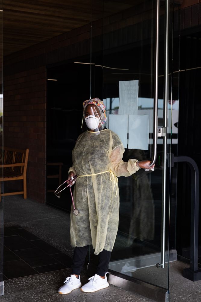 Full length shot of nurse in PPE with stethoscope holding door to doctor office open