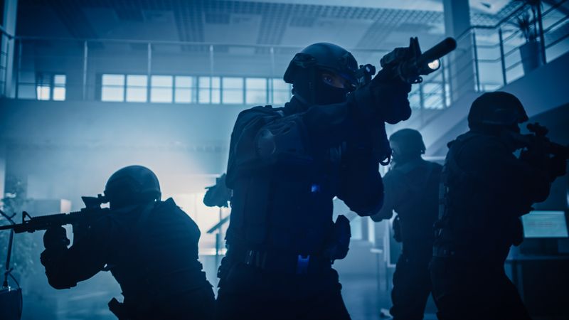 Masked Squad of Armed SWAT Police Officers Stand in Dark Seized Office Building with Desks and Computers.