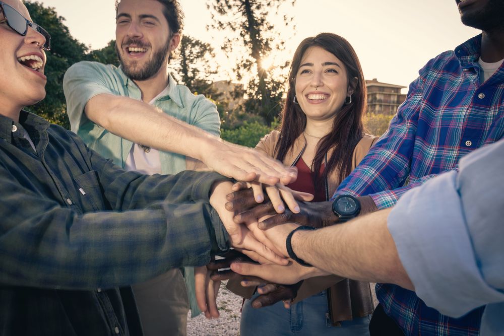 Close-up of a diverse group of happy friends putting their hands together in a huddle.