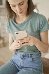 Relaxed women sitting on washing machine and browsing smartphone