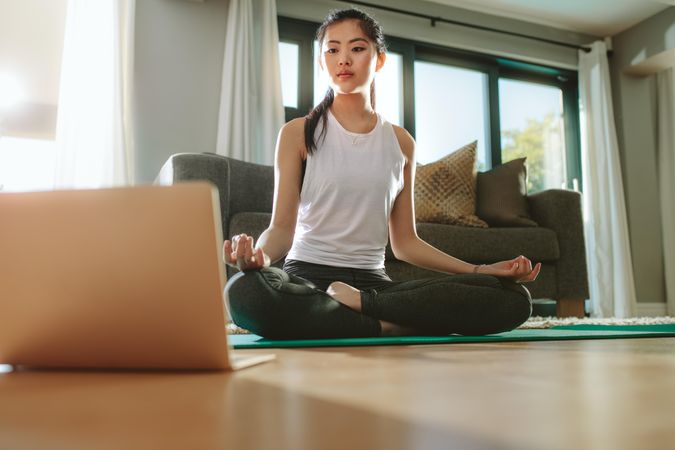 Chinese woman exercising yoga while watching instructional videos on laptop