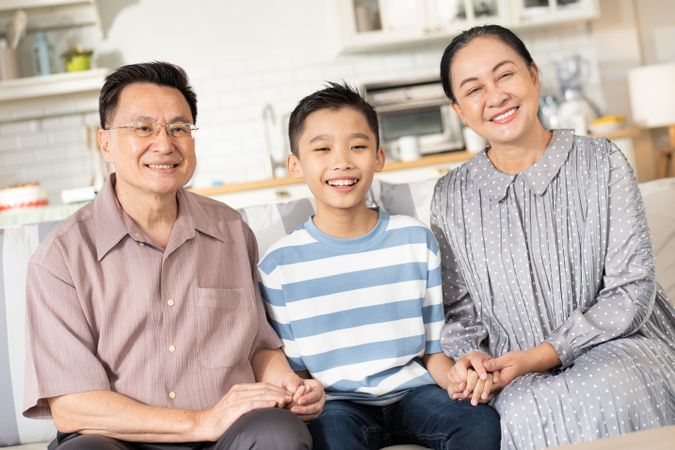 Happy Asian grandson and grandparents relax sitting on couch in the living room