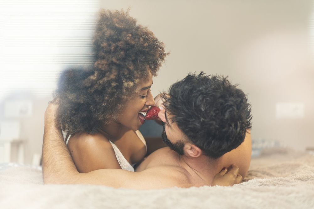 Happy couple eating strawberry on bed