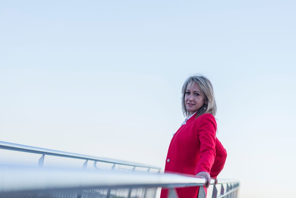 Woman in red coat leaning on railing of pedestrian bridge
