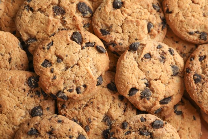Tasty chocolate chip cookies as background, top view