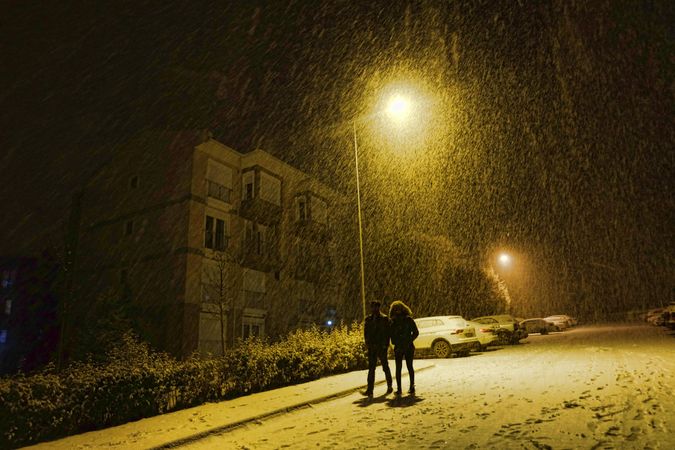 Silhouette of man and woman walking on the road during snowy night