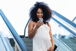 Pregnant Black woman browsing smartphone on escalator