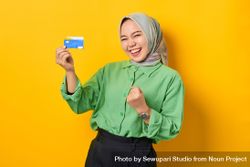 Muslim woman in headscarf and green blouse holding gift card she won 5oe7zb