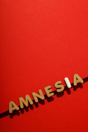 Cork letters of the word “Amnesia” with pill along bottom of red background, vertical composition
