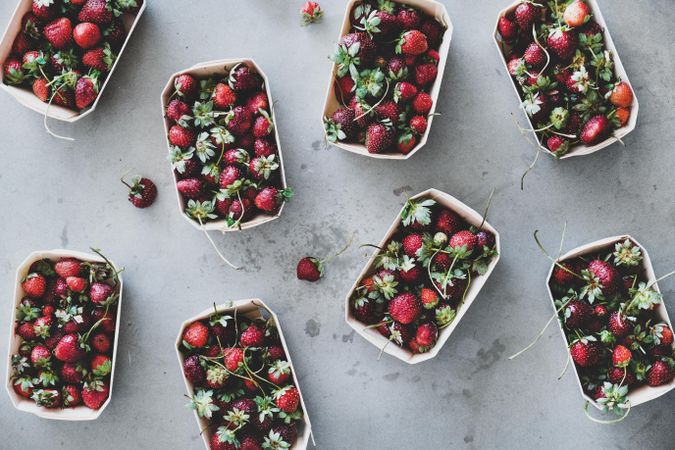 Strawberries in eco-friendly plastic-free boxes, scattered on concrete background