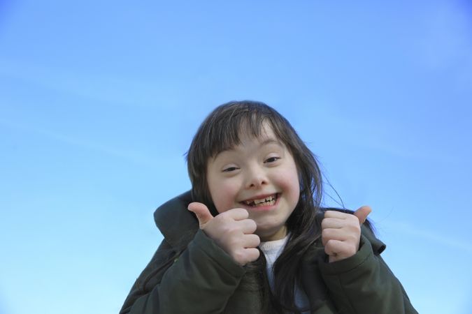 Little girl giving a thumbs up and smiling against a bright blue sky